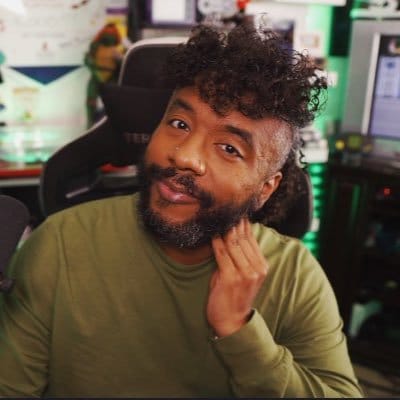 @okaydrian wearing a green long sleeved shirt looking happily at the camera sitting in a gaming chair